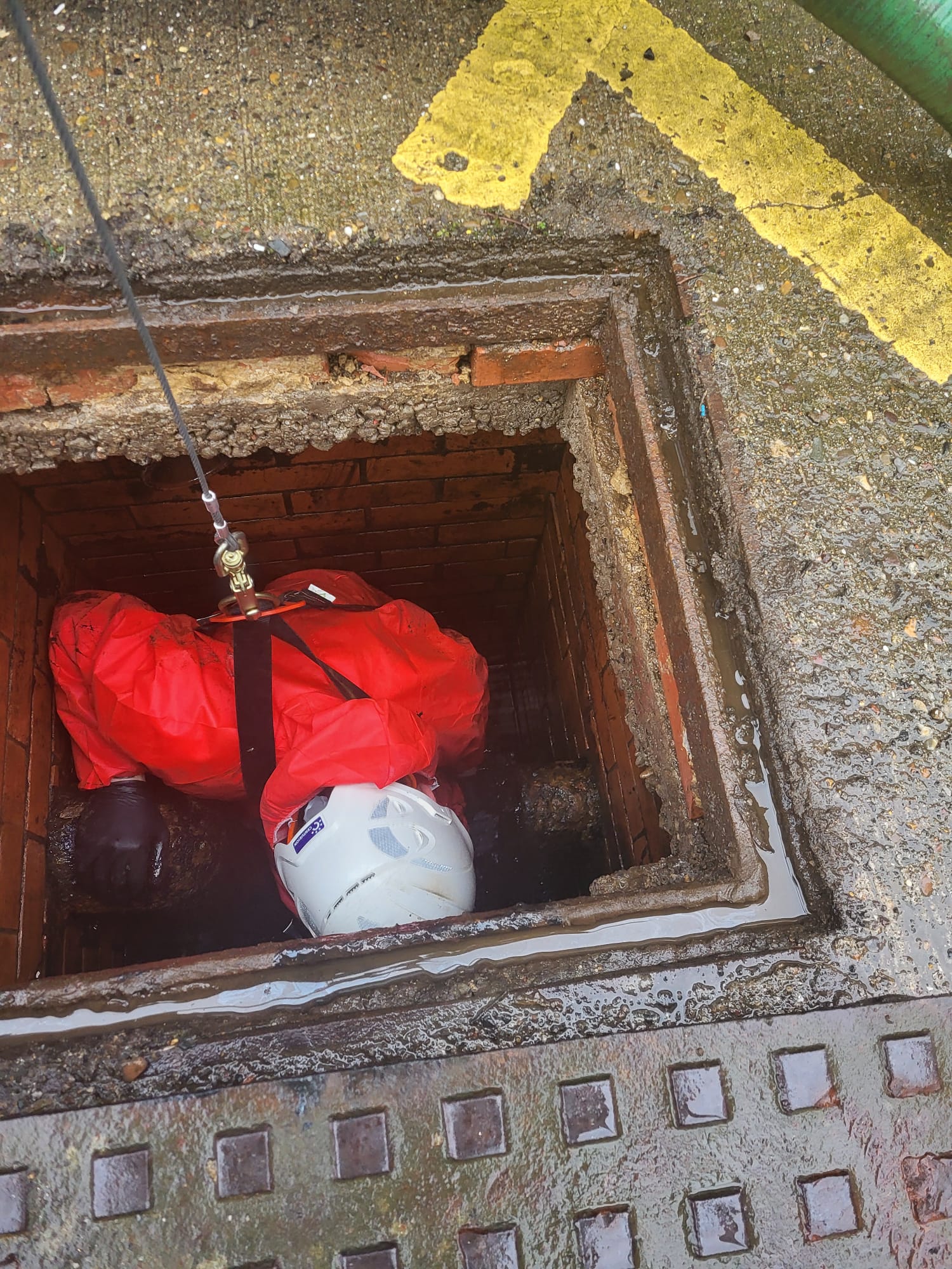 engineer in red coveralls and white hard hat in a large outside drain