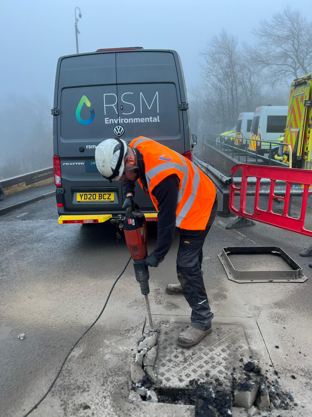 engineer jackhammering around a manhole cover on a street in front of an RSM van